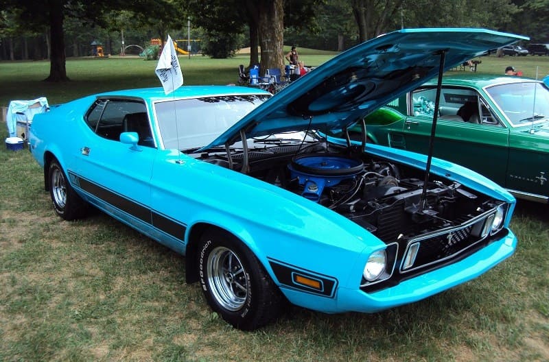 A classic light blue Ford Mustang on display with the hood up 