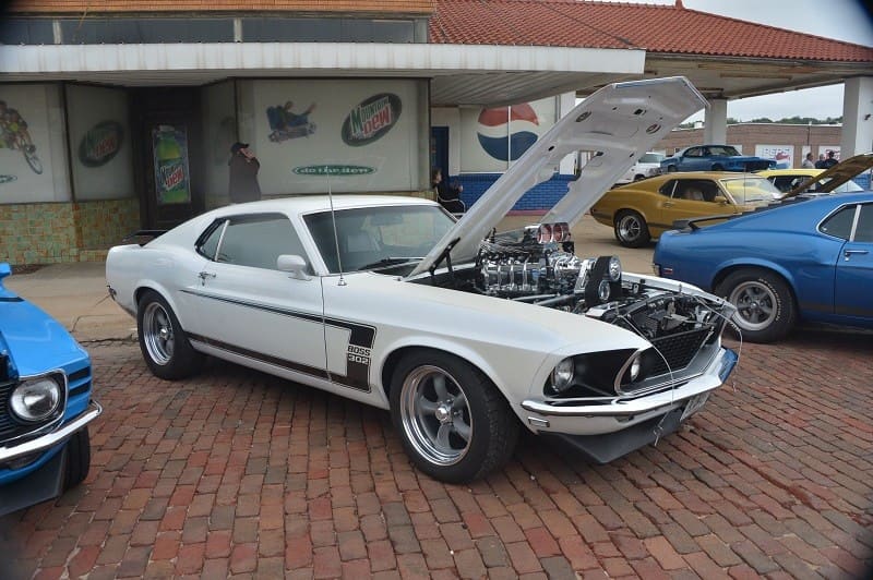 A front side view of a classic white Ford Mustang on display with the hood up 