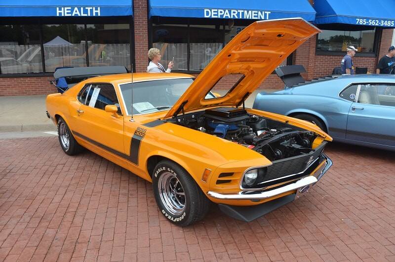 A classic orange Ford Mustang on display with the hood up 