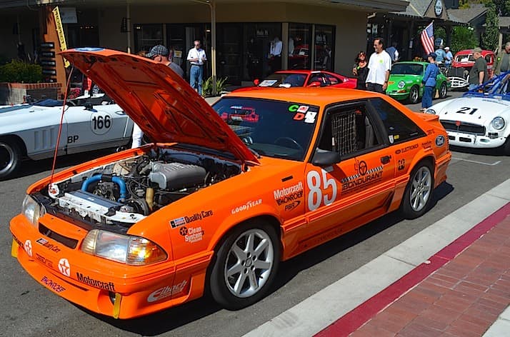 An orange Mustang GT on display with the hood up 