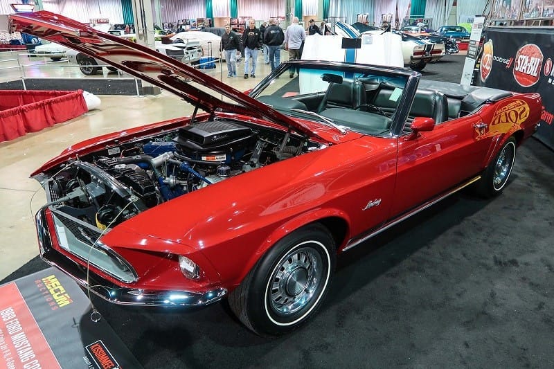 A front side view of a red Mustang on display with the hood up 
