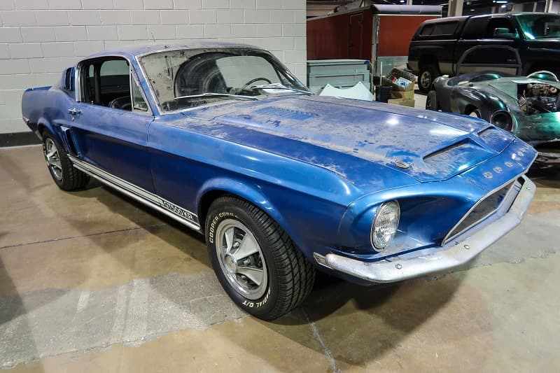A front side view of a dirty blue Mustang on display 