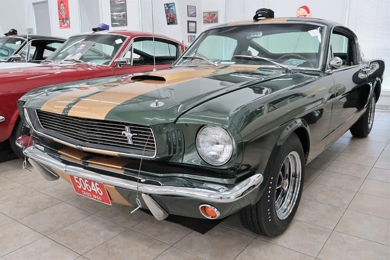 Front of a green Mustang with gold stripes parked inside building 