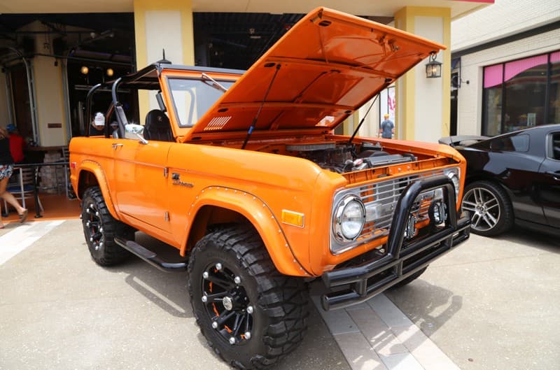 Front profile of an orange Bronco with the hood open in a parking lot