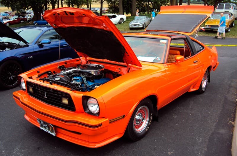 Front profile of a orange Shelby Mustang with hood and trunk open in a parking lot