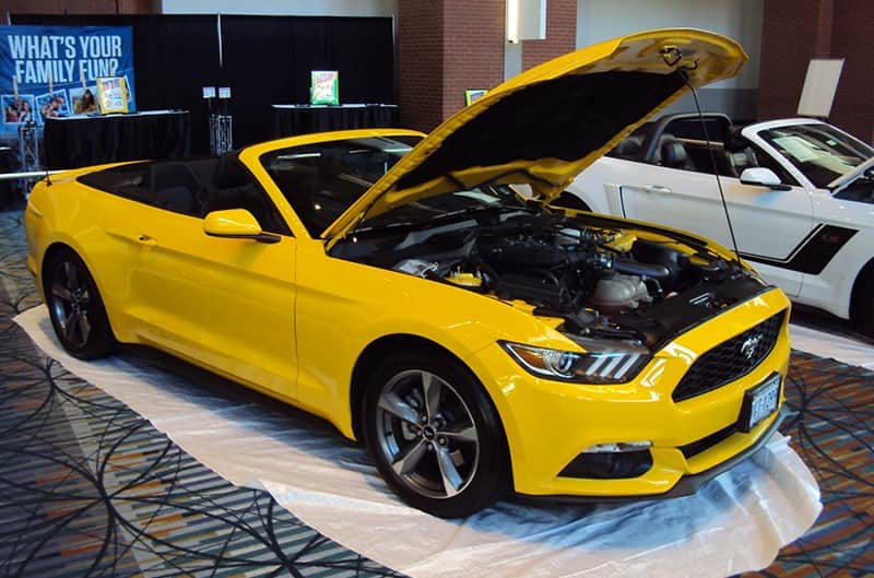 Front profile of a yellow Mustang convertible with hood open on display