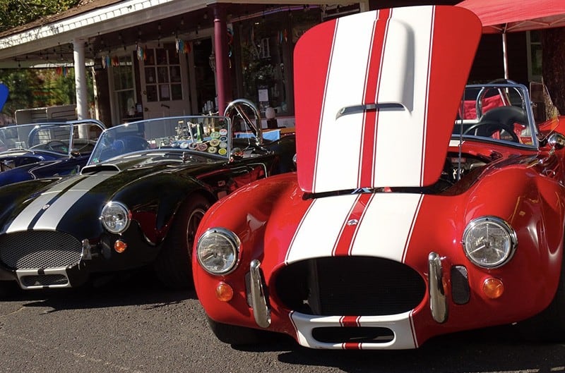 Two Shelby Cobras parked with hoods open