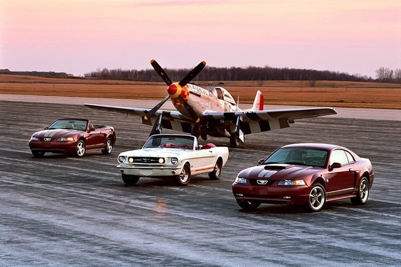 Three Mustangs on display in front of a small plane 