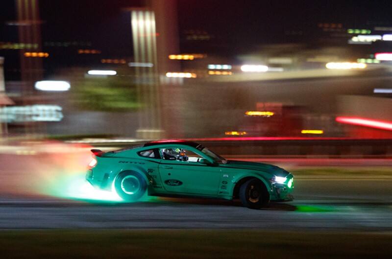 A side view of Gittin Jr. speeding through a cloverleaf interchange at night in his bright green Ford Mustang RTR 